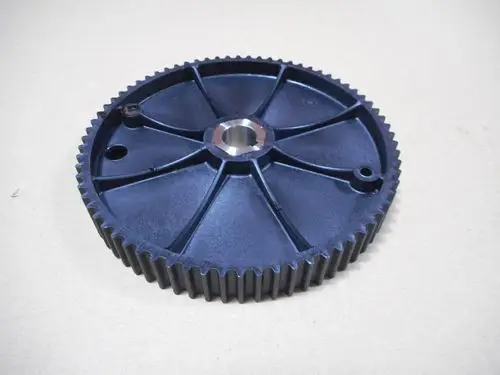 Schwarzes Zahnrad mit Rippenprofil und zentralem Loch, produziert von Remeha. Sichtbare Öffnungen an der Seite zur Befestigung oder Führung von Mechanismen.